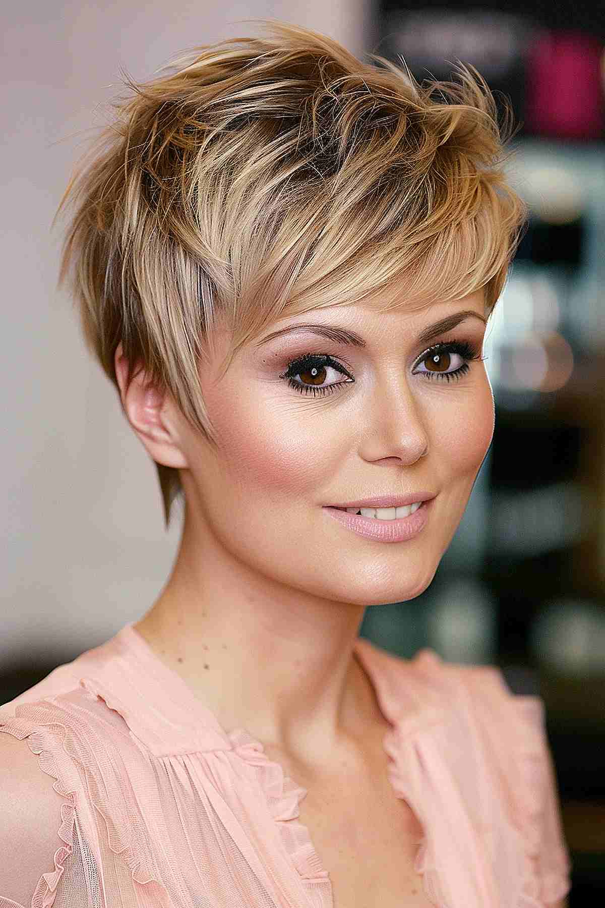 Woman with a blonde layered feathered pixie cut, offering volume and an elongated look for round face shapes, highlighted with blonde tones.